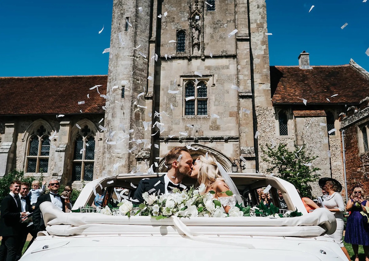Wedding couple kissing in wedding car outside St Cross chapel